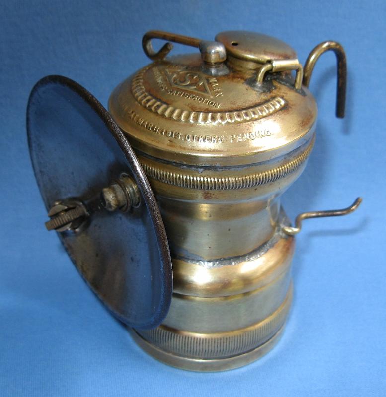 Simmons Intermediate LSide.JPG - SIMMONS INTERMEDIATE STYLE LAMP - Brass intermediate style lamp by John Simmons Co., top marked S in diamond trade mark, PAT. DEC 17, 1901, BALDWIN PAT. MAR 11, 1913, OTHERS PENDING, with 2 5/8 in. tinned screw on steel reflector, Simmons No. 32 lamp  [The Simmons intermediate style lamp represents a transition from the Simmons Pioneer lamp to later lamps such as the ITP and Sun-Ray lamps manufactured by the Dewar Co. after they took over production of the Simmons lamps. The John Simmons Co. manufactured its own cap and superintendent-style lamps marked with the distinctive raised S in a diamond trade mark. One of the last lamp models marketed by Simmons was the Pioneer, first advertised around 1917. The patent dates marked on these lamps are for patent No.688,926 awarded to A. L. Buffington on Dec. 17, 1901 for an acetylene bicycle lamp with burner and reflector on the same axis and design patent No.13,542 awarded to Baldwin on Mar. 11, 1913 for an acetylene generating lamp. These lamps (as shown elsewhere in my pics) were joined by a new cap lamp as shown here and first advertised in 1918.  This lamp was designated as a No. 32 by Simmons and unlike the Pioneer lamp, it included wire cap braces and a newer water tank design patented by the Chase Brass Co. of Waterbury, CT.  This design patent was filed on Oct. 28, 1919 and awarded to H. T. Sperry, assignor to the Chase Companies, as No. 54,787 on Mar. 23, 1920. These intermediate style Simmons lamps, which include screw on reflectors and distinctive knurling around the top of the water tank, are quite uncommon and are among the last lamps marketed by Simmons before Dewar took over Simmons lamp production in 1919.  Dewar took possession of the remaining Pioneer stock and advertised these lamps along with their own brands of the ITP and Sun-Ray lamps.  See Thorpe, Carbide Light, pp 45-47]